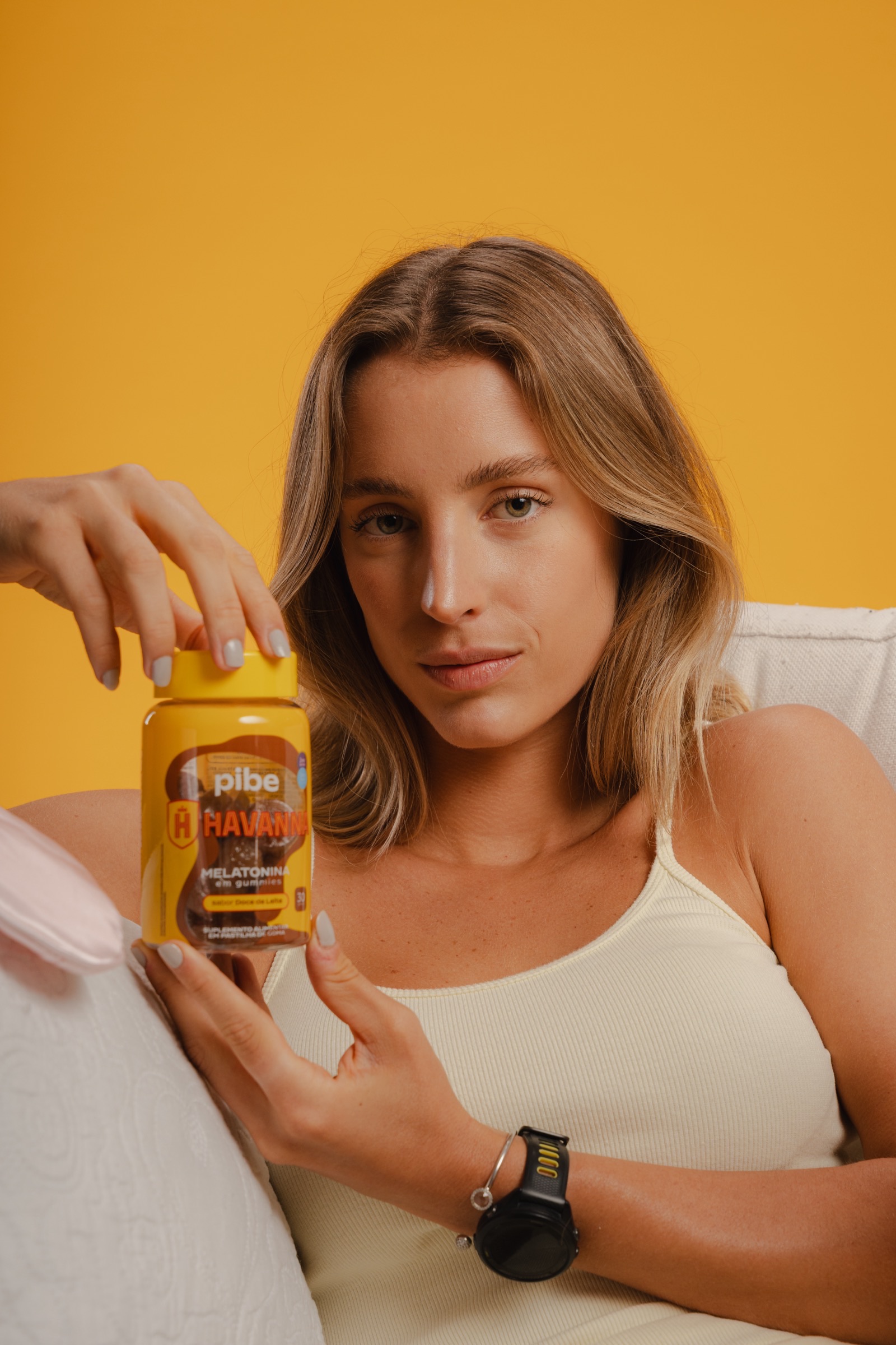 Mulher sentada segurando o pote de Pibe Havanna Melatonina em gummies sabor doce de leite